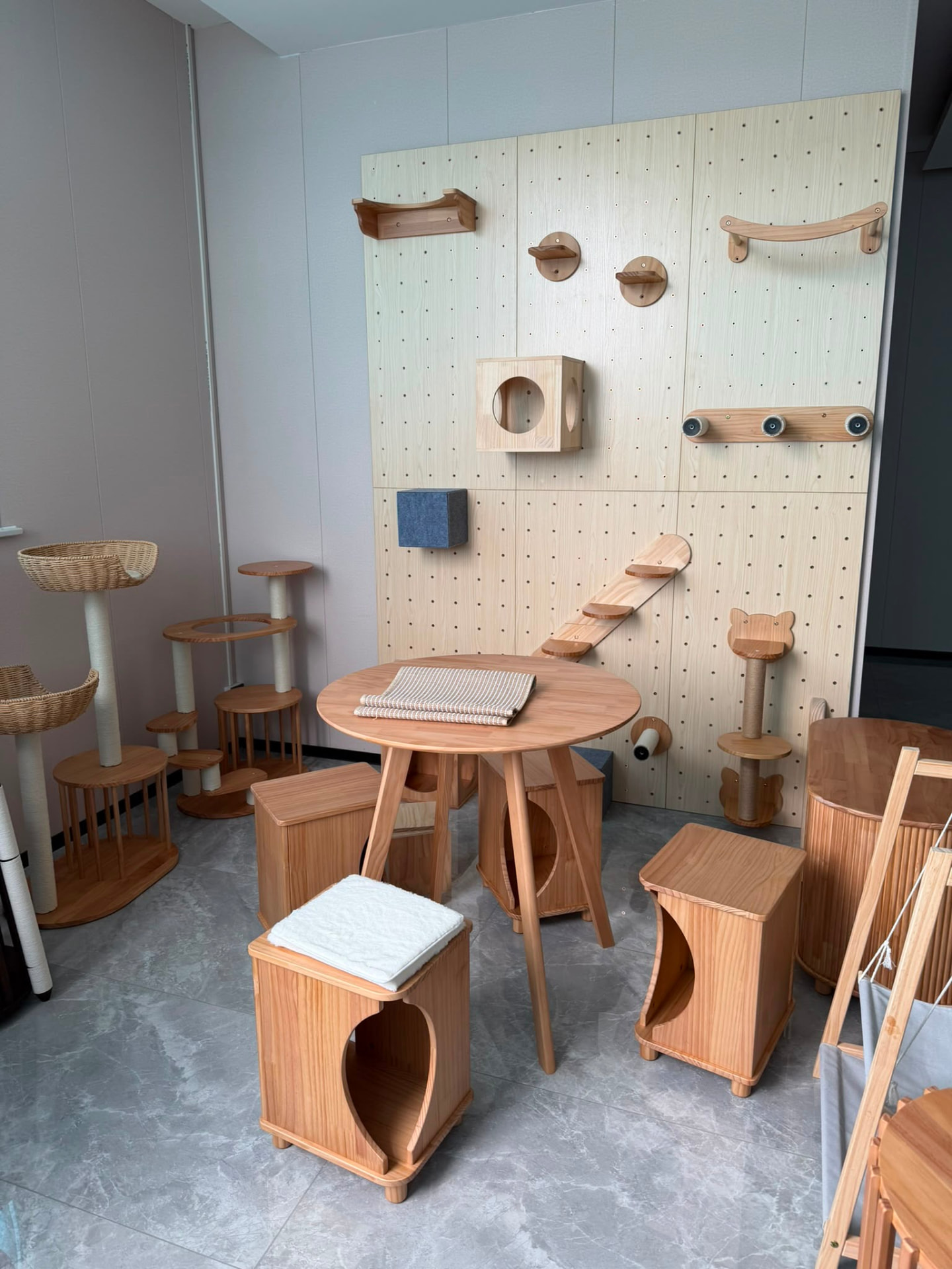 Round solid wood cat table with hideaway stools in front of a cat climbing pegboard
